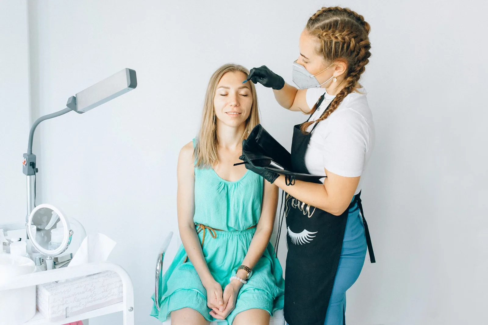 A trained beautician performs eyebrow microblading on a client in a professional salon.