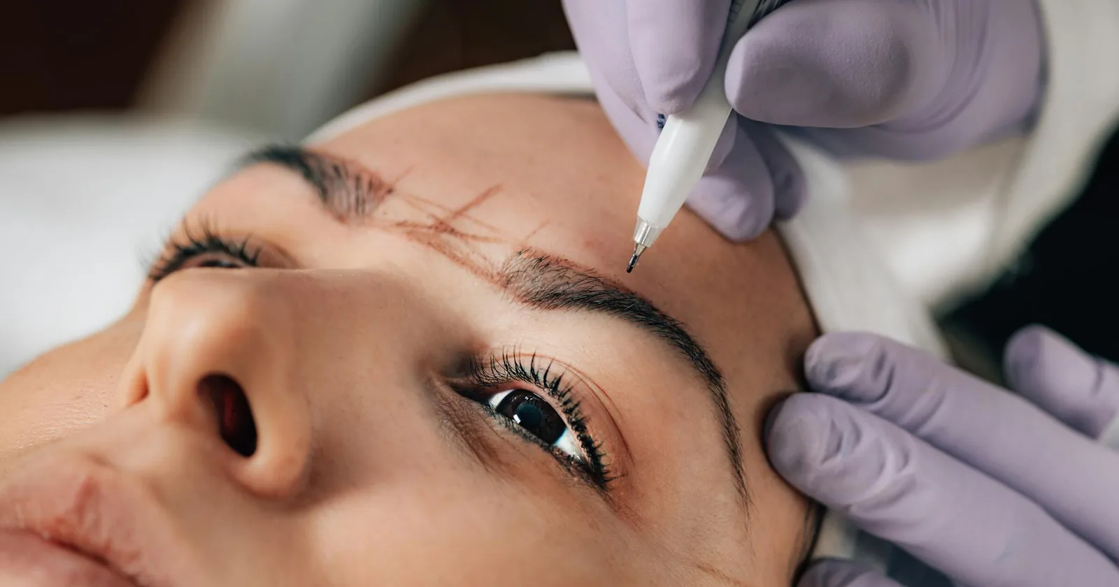 A beautician performs precise microblading on a client's eyebrows in a salon.