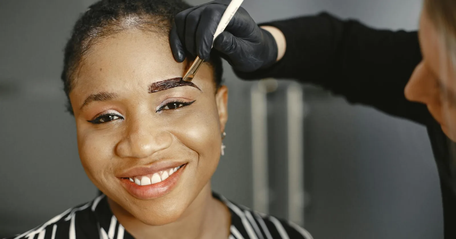 A woman enjoys her eyebrow treatment with a smile, showcasing beauty and self-care.