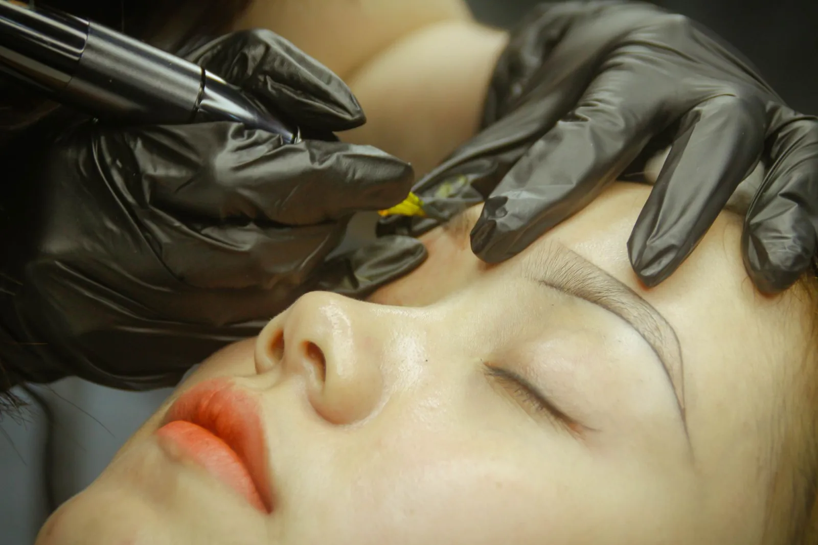 A close view of an eyebrow microblading procedure performed with gloved hands.