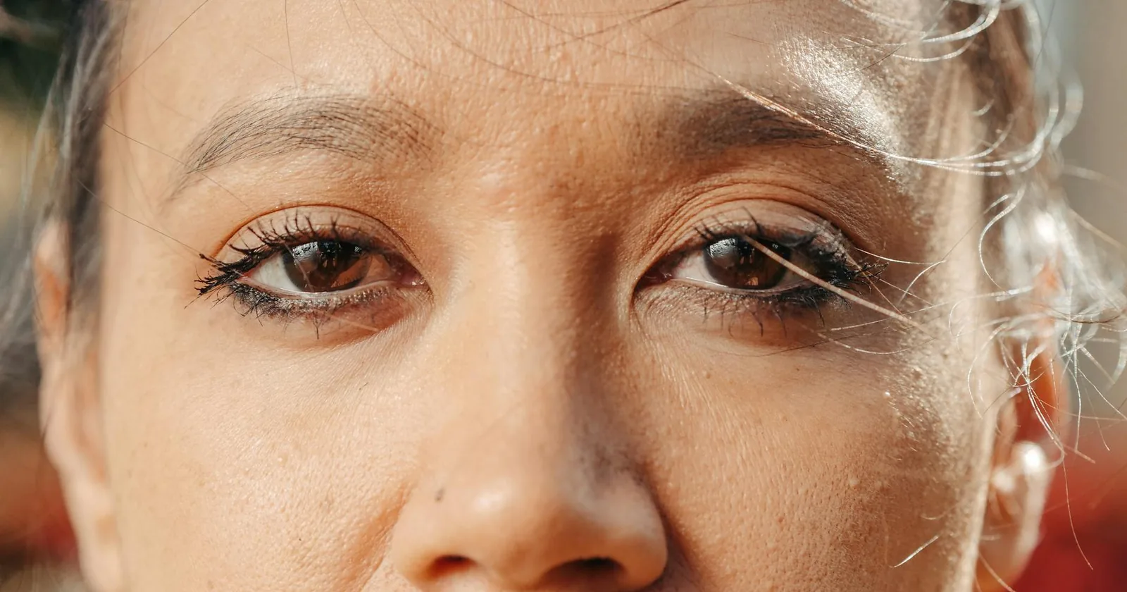 Extreme close-up of a woman's eyes with soft natural lighting, showing eye makeup and skin texture.