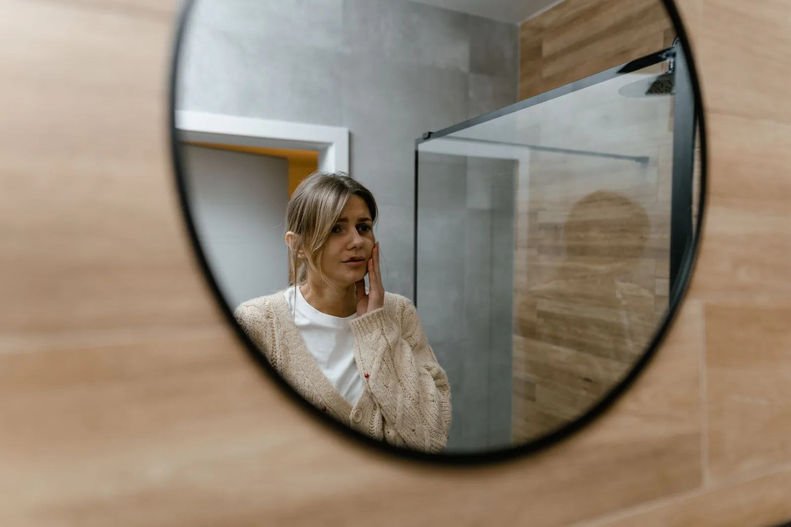 A woman looking at her reflection in a round bathroom mirror