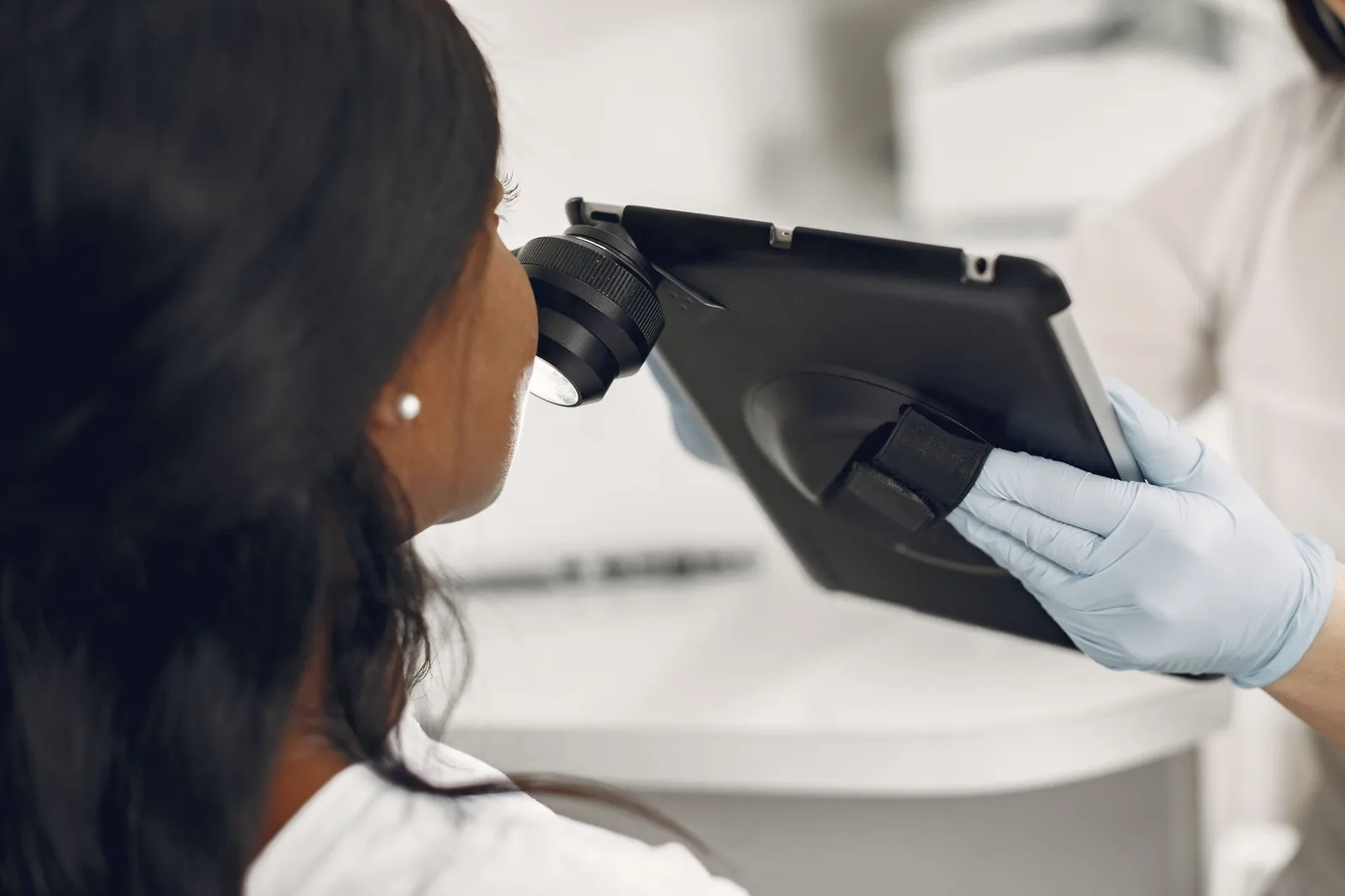 A gloved clinician examining a patient's skin with a dermatoscope
