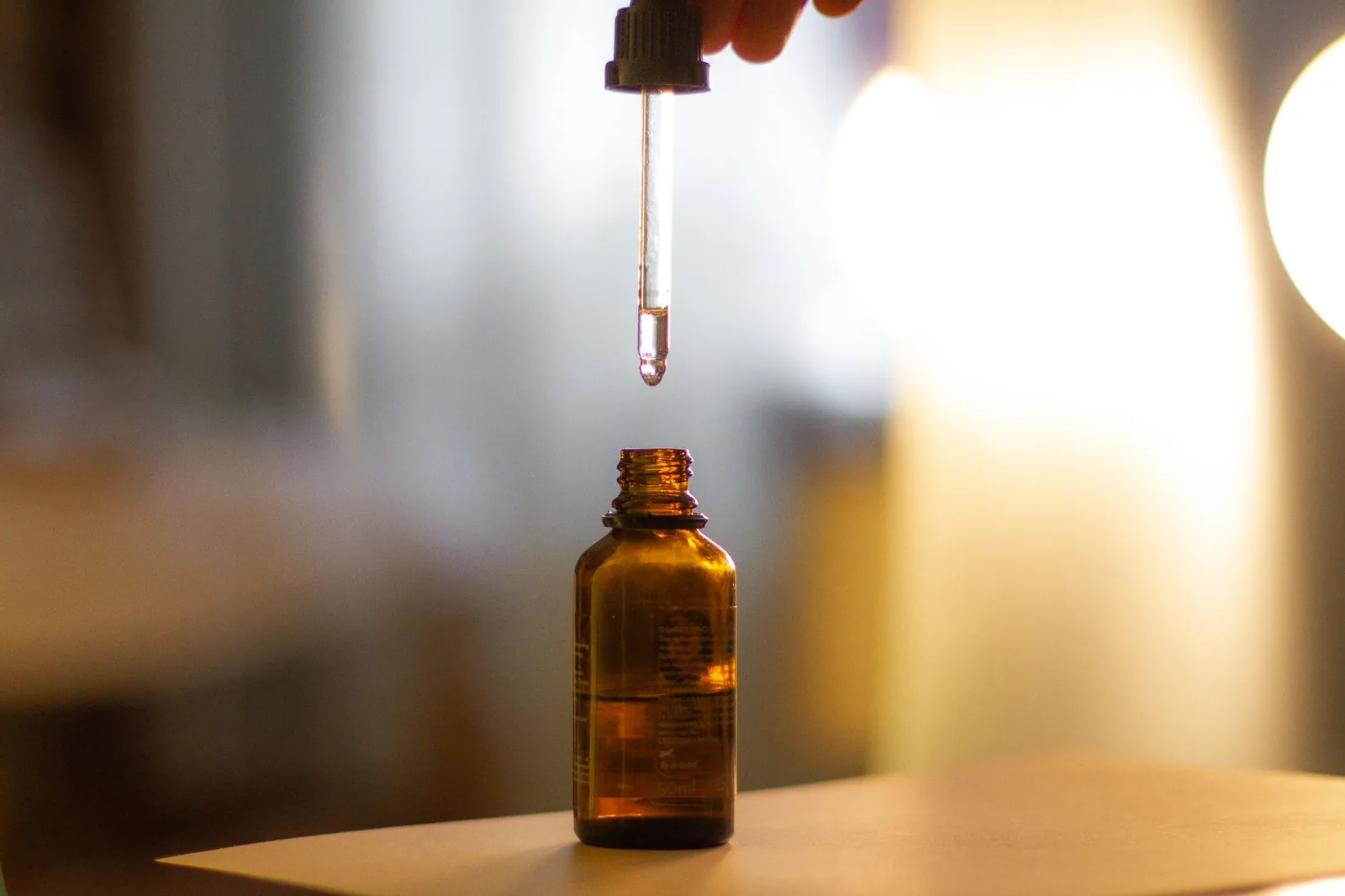 A serum dropper held above an amber glass bottle, lit softly against a blurred background.