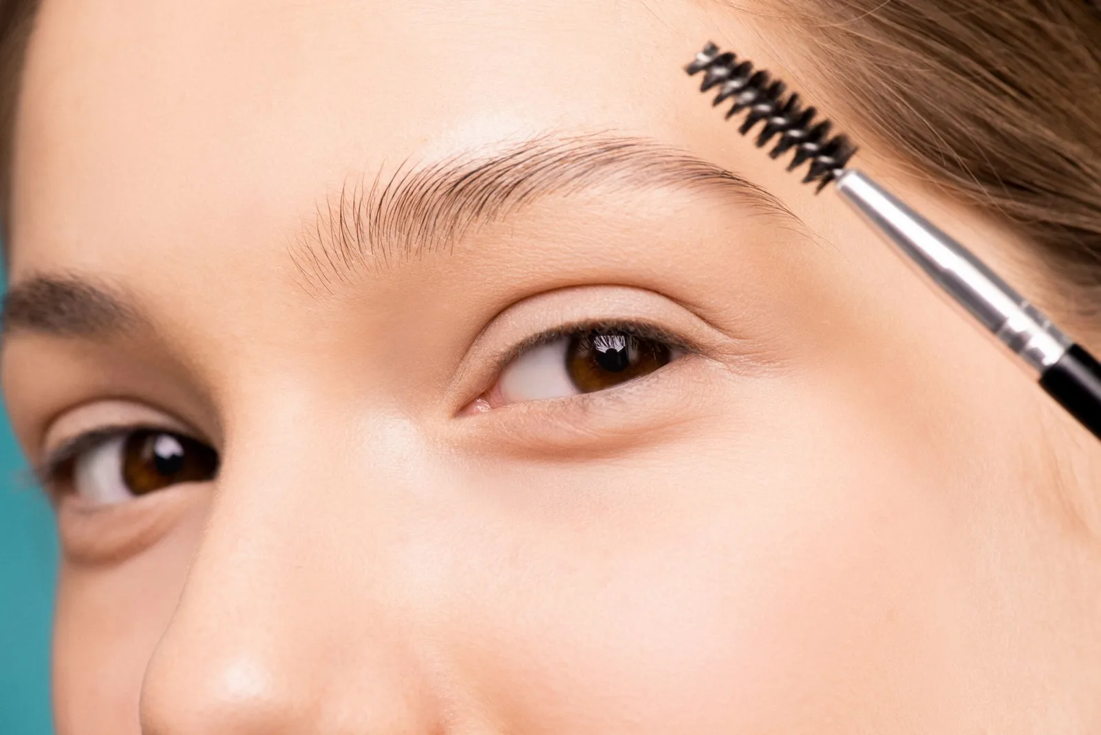 Close-up of a woman grooming her eyebrow with a small brush.