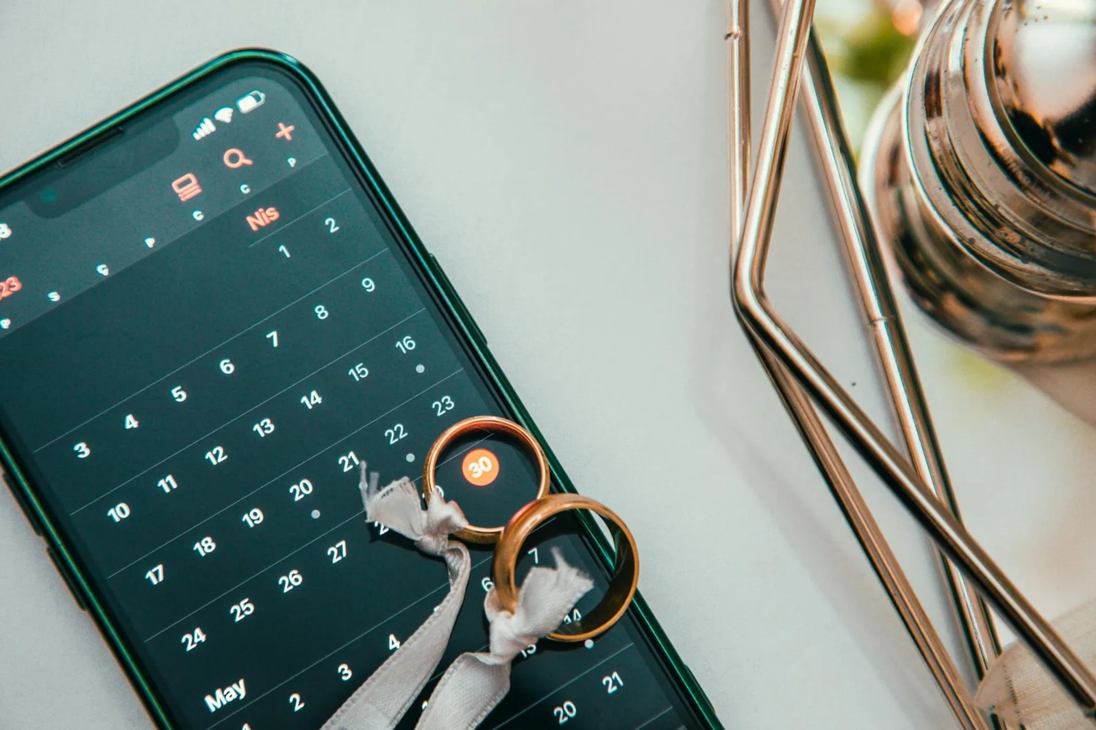 Wedding rings resting on a smartphone displaying a calendar, symbolizing the planning of a wedding date.